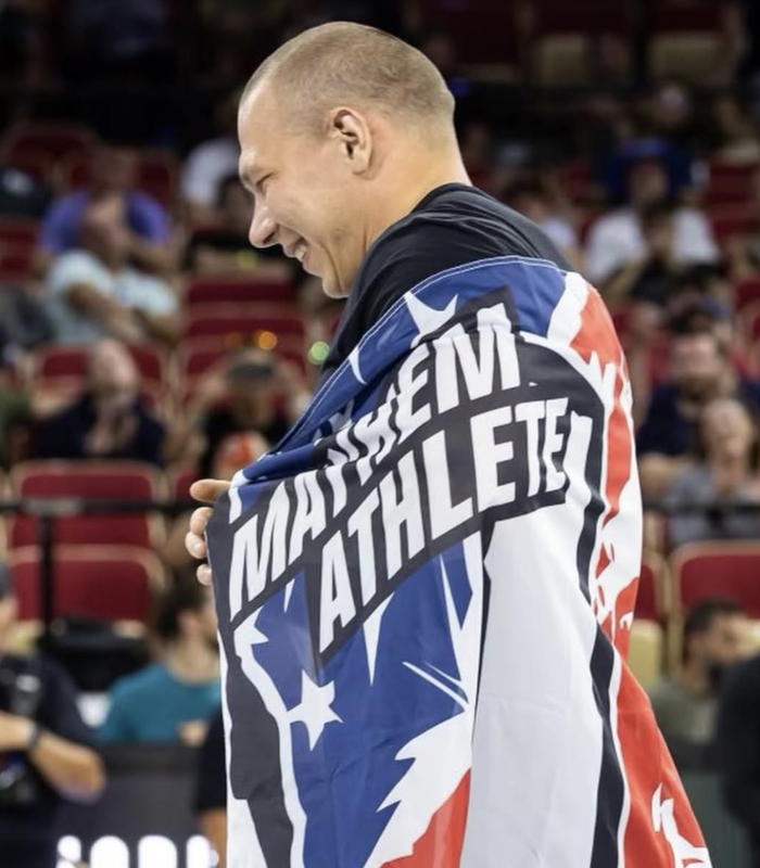 Roman Khrennikov smiling while wrapped in a Mayhem Athlete flag